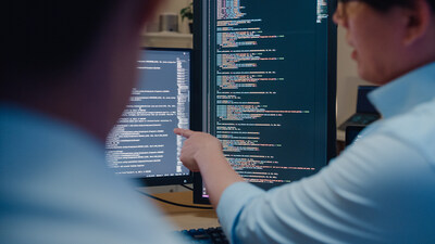 Closeup group of Asian people software developers using computer to write code sitting at desk with multiple screens in office at night. Programmer development concept.